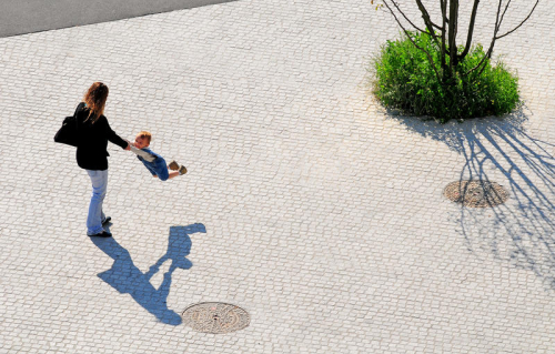 Photo d'une femme jouant avec son enfant sur une place en pavés.